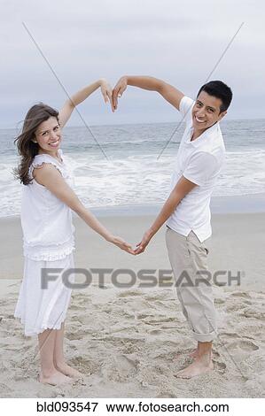 Hispanic couple making heart shape with arms on beach View Large Photo Image Stock Photo - Hispanic couple making heart shape with arms on beach. Fotosearch