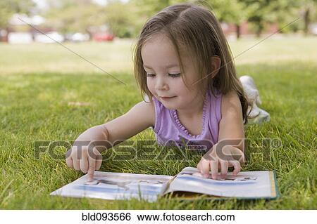 Stock Photograph - Hispanic girl laying in grass reading book. Fotosearch
