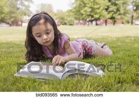 Stock Photography - Hispanic girl laying in grass reading book. Fotosearch
