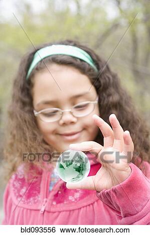 Stock Photograph - Hispanic girl looking at small glass globe. Fotosearch