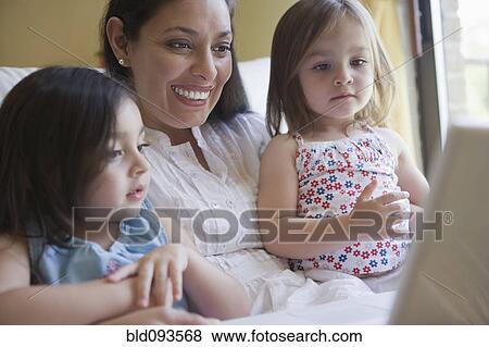 Stock Photo - Hispanic mother and daughters using laptop together. Fotosearch