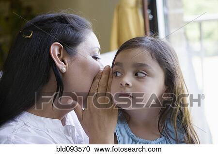 Stock Image - Hispanic mother whispering to daughter. Fotosearch