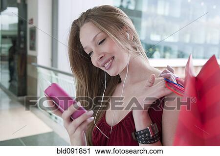 Stock Image - Hispanic woman carrying shopping bags listening to mp3 player. Fotosearch