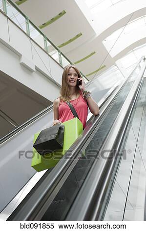 Hispanic woman carrying shopping bags and using cell phone on escalator View Large Photo Image Stock Photography - Hispanic woman carrying shopping bags and using cell phone on escalator. Fotosearch