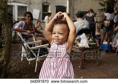 Stock Image - Mixed race baby girl standing on patio with arms raised. Fotosearch