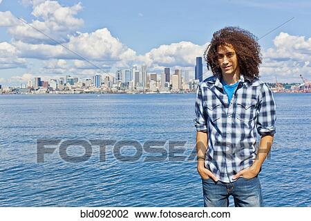 Stock Image - Mixed race teenager standing at urban waterfront. Fotosearch