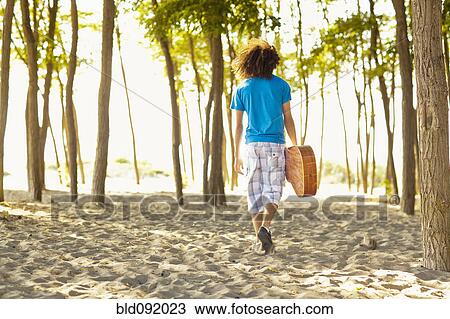 Stock Image - Mixed race teenager walking in sand carrying guitar. Fotosearch