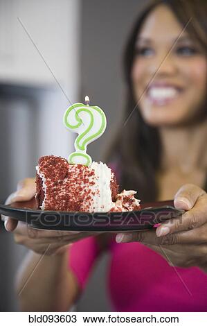 Stock Image - Mixed race woman holding cake with question mark candle. Fotosearch