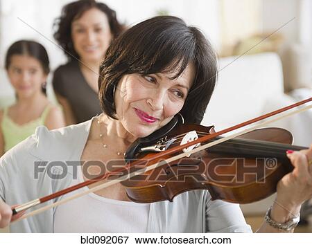 Stock Photo - Mother and daughter watching grandmother playing violin. Fotosearch