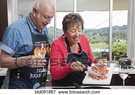 Stock Photo - Senior Hispanic couple cooking together in kitchen. Fotosearch