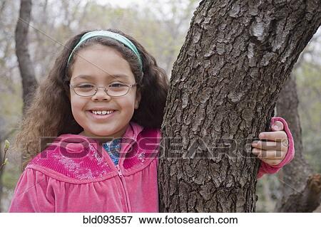 Stock Photo - Smiling Hispanic girl hugging tree trunk. Fotosearch