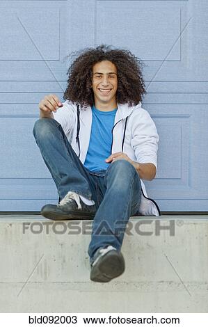 Stock Image - Smiling mixed race teenager sitting outdoors. Fotosearch