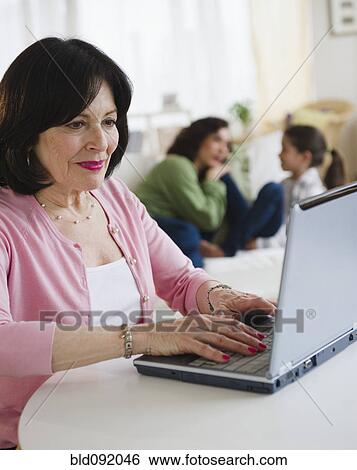 Woman using laptop with family in background View Large Photo Image Stock Photograph - Woman using laptop with family in background. Fotosearch