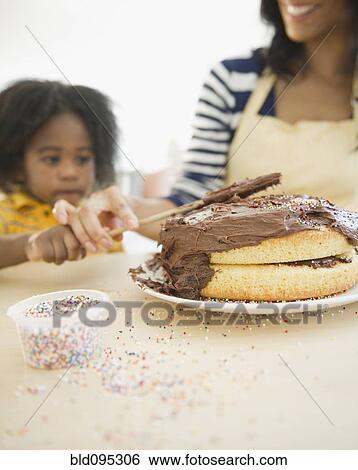 Stock Photograph - African American mother and son icing cake. Fotosearch