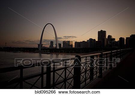Stock Photograph - Arch landmark next to urban river at sunset. Fotosearch