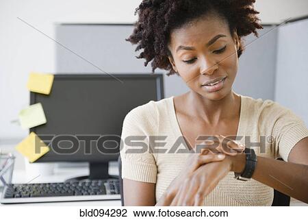 Stock Image - Black businesswoman checking the time at desk. Fotosearch