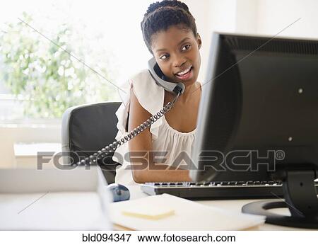 Stock Photo - Black businesswoman talking on phone and using laptop. Fotosearch