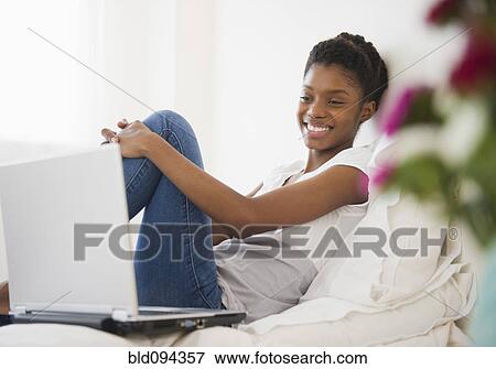 Stock Photo - Black woman laying in bed using laptop. Fotosearch