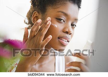 Picture - Black woman putting on face lotion. Fotosearch
