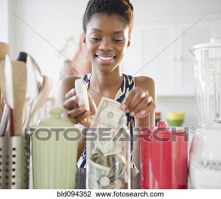 Stock Image - Black woman taking money out of jar. Fotosearch