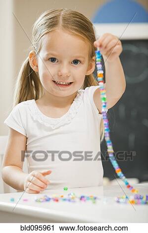 Stock Image - Caucasian girl stringing beads. Fotosearch