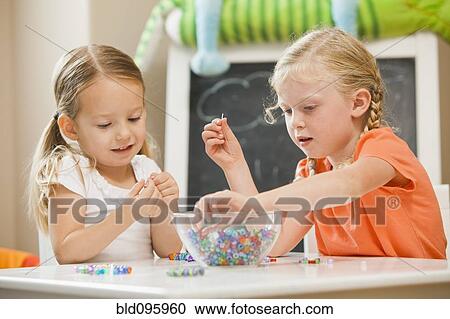 Stock Image - Caucasian sisters playing with beads. Fotosearch