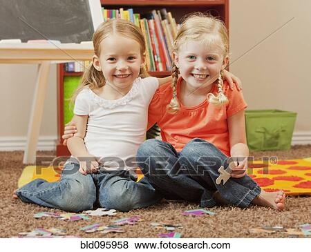 Stock Photo - Caucasian sisters putting together puzzle. Fotosearch