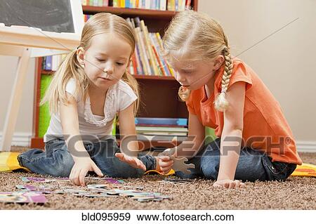 Stock Photo - Caucasian sisters putting together puzzle. Fotosearch