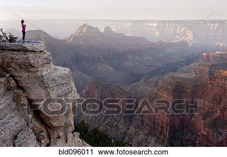 Stock Image - Caucasian woman practicing yoga on cliff near canyon. Fotosearch