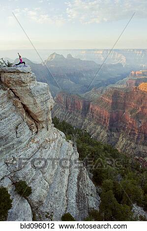 Stock Image - Caucasian woman practicing yoga on cliff near canyon. Fotosearch