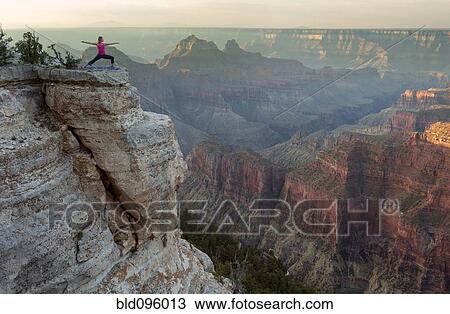 Stock Image - Caucasian woman practicing yoga on cliff near canyon. Fotosearch