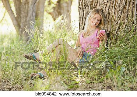Stock Image - Caucasian woman sitting in grass and text messaging. Fotosearch