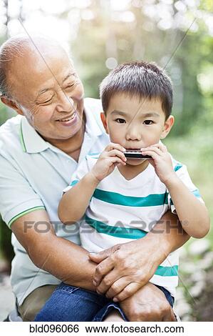 Stock Photograph - Chinese grandfather watching grandson with harmonica. Fotosearch