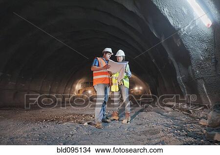 Picture - Construction workers looking at blueprint in tunnel. Fotosearch