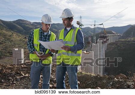 Stock Photo - Construction workers looking at blueprint at construction site. Fotosearch