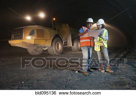 Construction workers looking at blueprint in tunnel View Large Photo Image Stock Photograph - Construction workers looking at blueprint in tunnel. Fotosearch