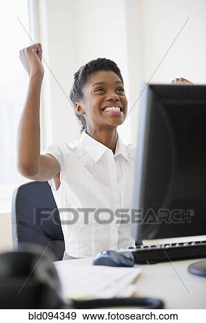 Excited Black businesswoman cheering at desk View Large Photo Image Stock Photo - Excited Black businesswoman cheering at desk. Fotosearch