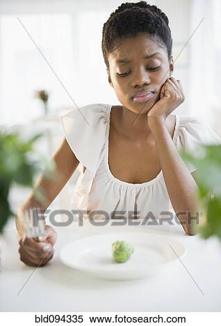 Stock Photography - Frustrated Black woman looking at brussels sprout. Fotosearch