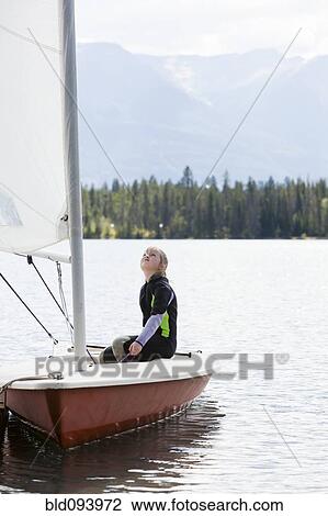 Stock Image - Girl sitting in sailboat looking up. Fotosearch