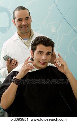 Stock Image - Hispanic Barber listening to client in barber shop. Fotosearch