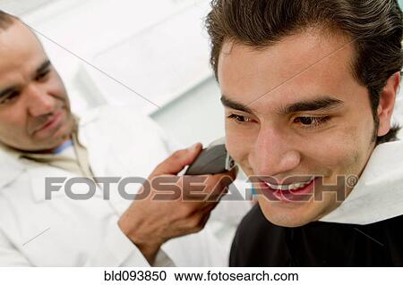 Stock Image - Hispanic Barber shaving man's neck in barber shop. Fotosearch