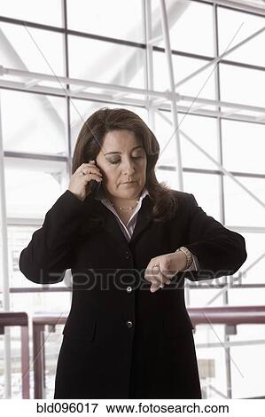 Stock Photo - Hispanic businesswoman talking on cell phone checking the time. Fotosearch