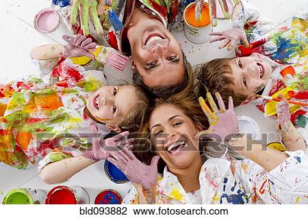 Stock Image - Hispanic family covered in paint laying on floor. Fotosearch