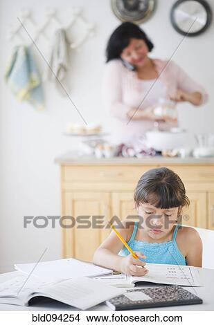 Picture - Hispanic girl doing homework with mother in background. Fotosearch
