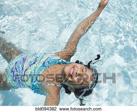 Stock Image - Hispanic girl floating in swimming pool. Fotosearch