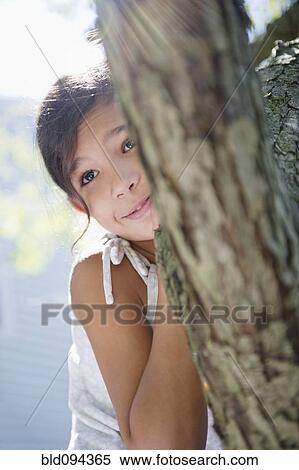 Stock Photography - Hispanic girl hiding behind tree. Fotosearch