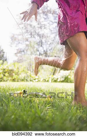 Stock Image - Hispanic girl running through sprinkler. Fotosearch