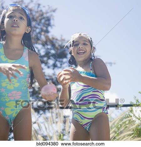 Stock Image - Hispanic girls in bathing suits playing with water balloons. Fotosearch