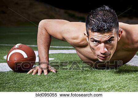 Stock Photography - Hispanic man doing push-ups near football. Fotosearch