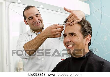 Stock Image - Hispanic man having hair cut in barber shop. Fotosearch